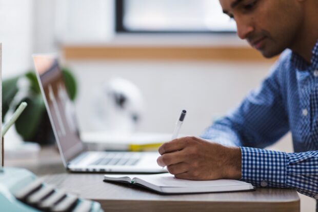 A man sat at a desk with a laptop and a notepad